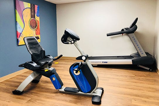 Light flooring, one blue wall, one white wall, an exercise bike, and a treadmill